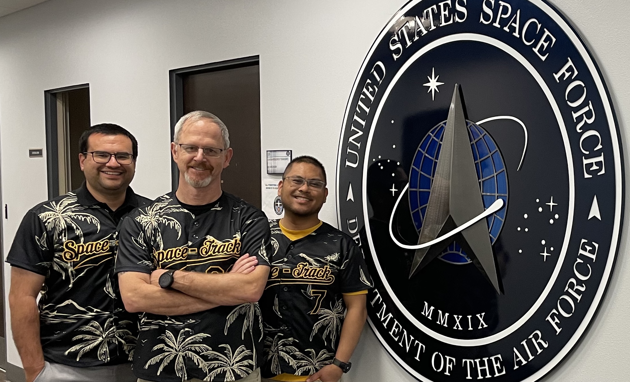 Rob with two Space-Track teammates beside the U.S. Space Force seal
